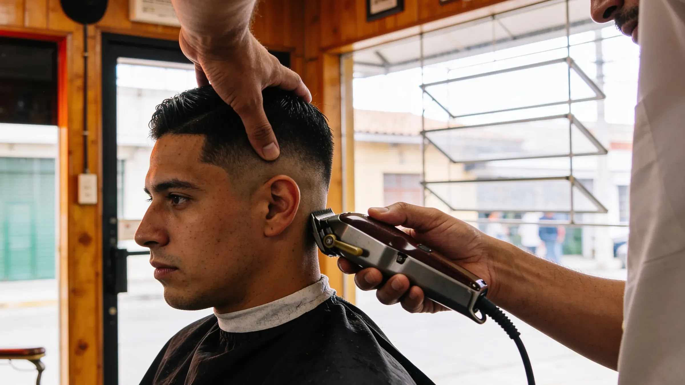 Manos de barbero trabajando un fade en una barbería mexicana cálida